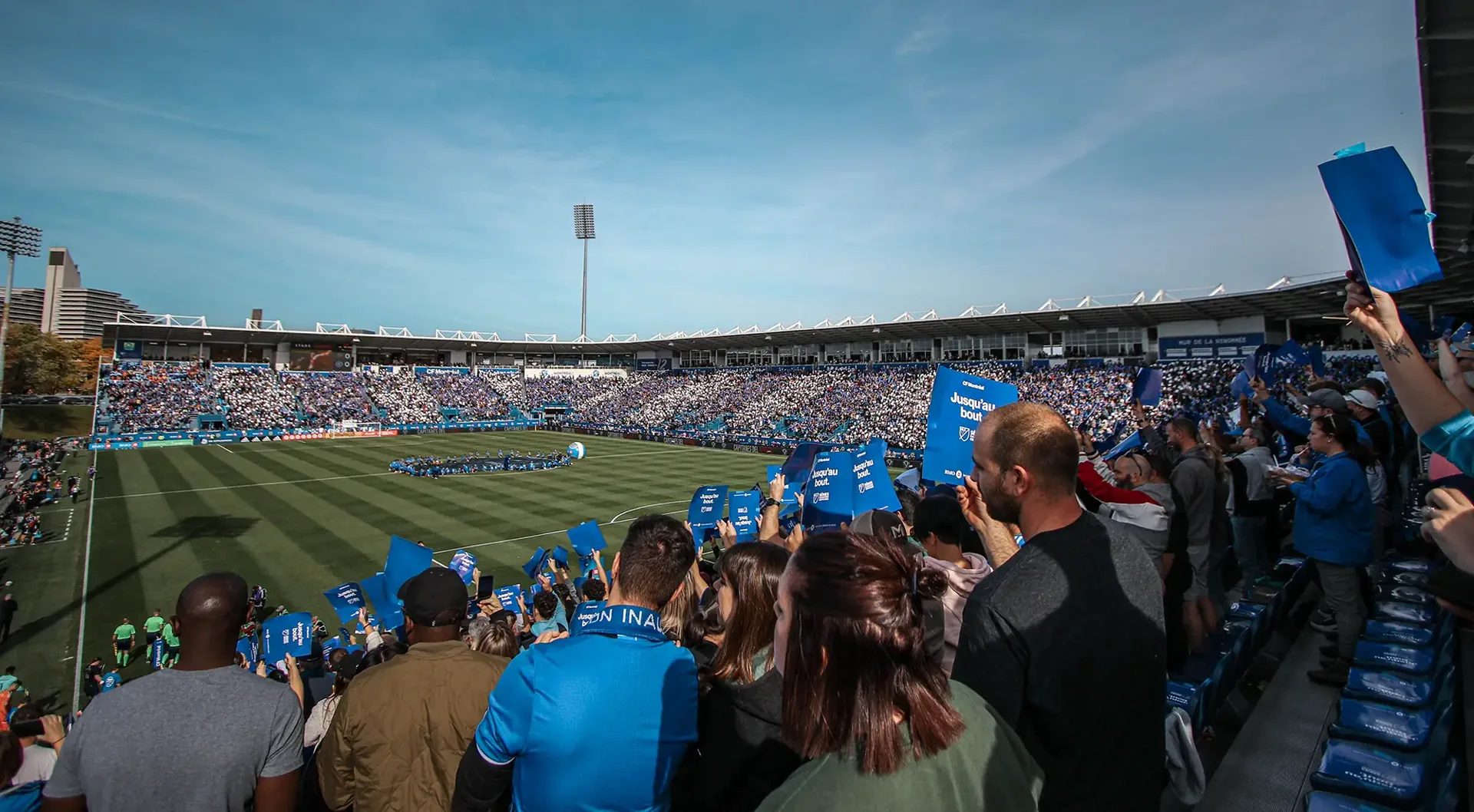 CF Montréal supporters holding blue cards reading Jusqu'au bout during a matchday display at Stade Saputo